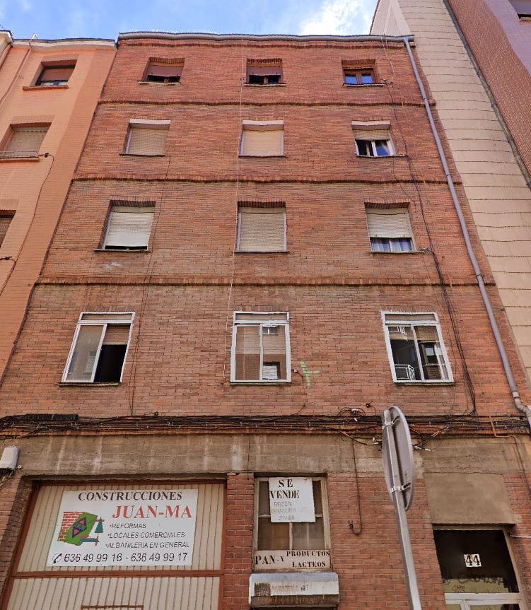 Weathered red brick residential building with multiple rows of windows and commercial signage at street level